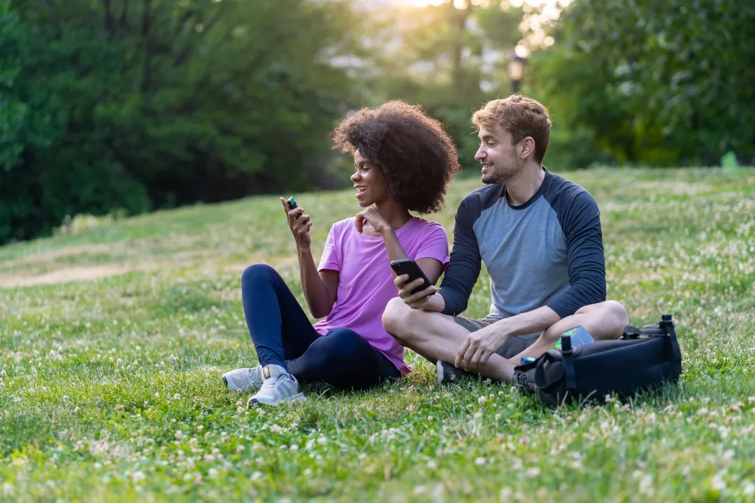A woman holding NICORETTE QuickMist sitting on the grass with a man holding his phone