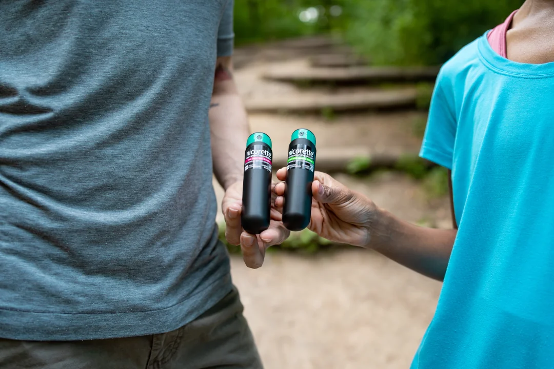 Two people each holding up a NICORETTE QuickMist Nicotine Spray